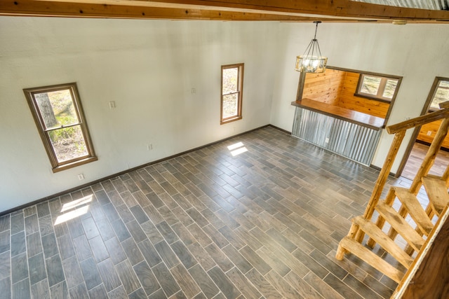 unfurnished living room with healthy amount of natural light, stairway, a chandelier, dark wood finished floors, and beam ceiling