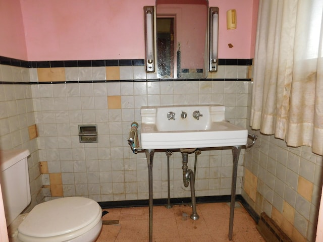 bathroom with tile walls, toilet, wainscoting, and a sink