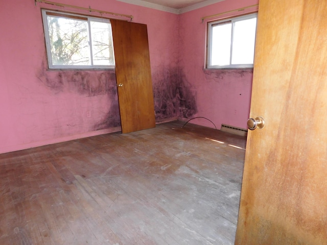 spare room featuring healthy amount of natural light, wood finished floors, and a baseboard heating unit