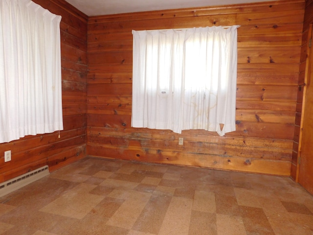spare room featuring light floors, wood walls, and a baseboard heating unit