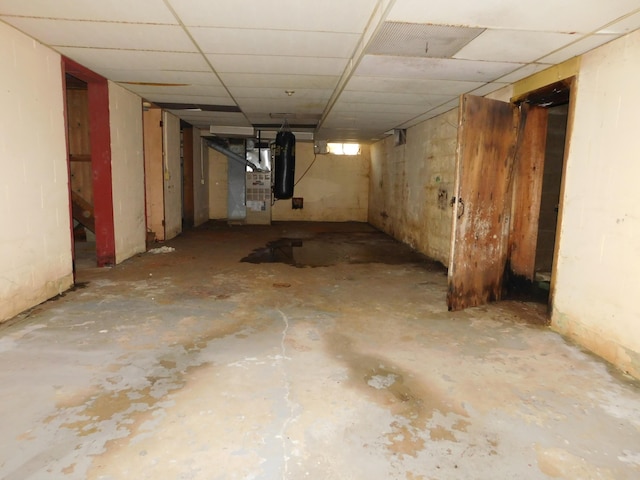 unfinished basement featuring a paneled ceiling and heating unit