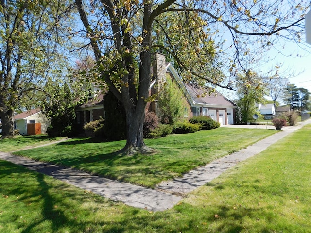 view of green lawn featuring an attached garage and driveway