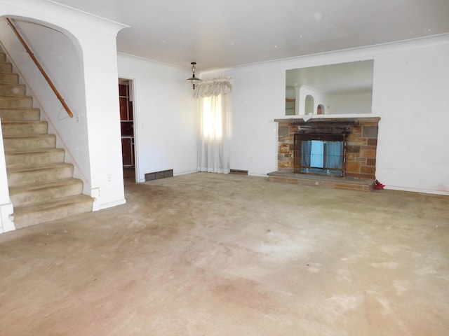 unfurnished living room with stairs, ornamental molding, and a stone fireplace