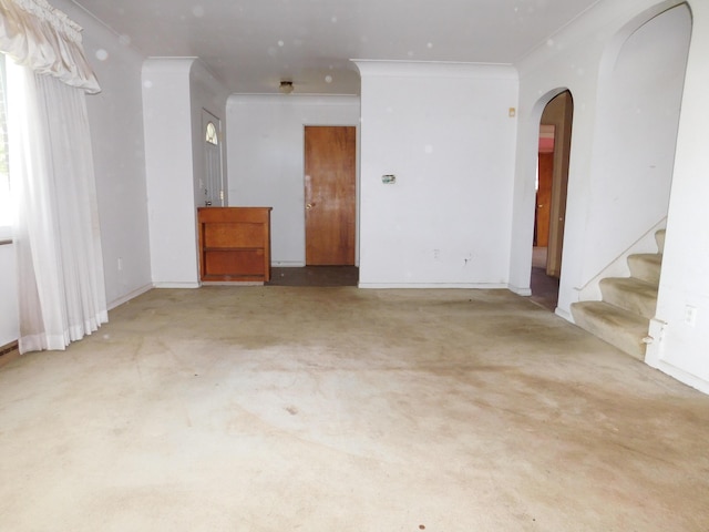 unfurnished room featuring arched walkways, stairs, ornamental molding, and baseboards