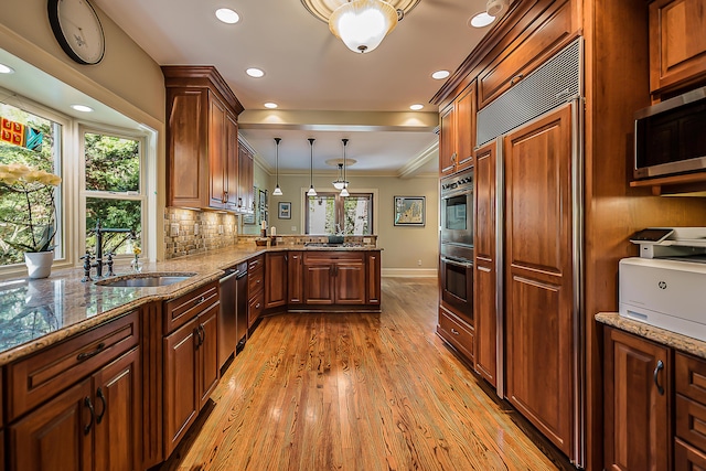 kitchen featuring a sink, a peninsula, stainless steel appliances, light wood-style floors, and hanging light fixtures