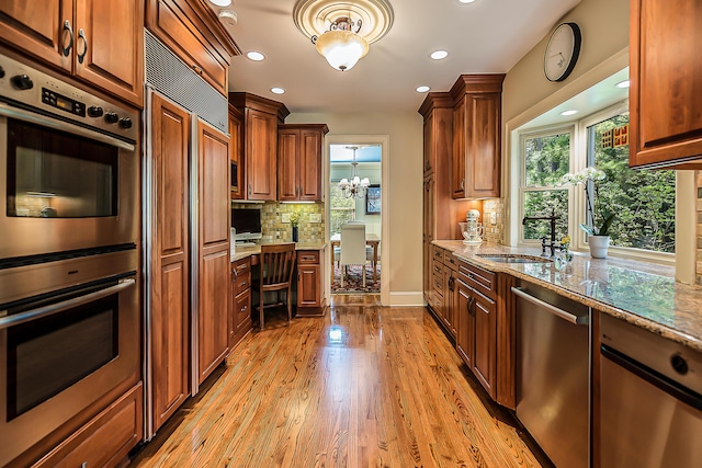 kitchen featuring stainless steel appliances, a sink, light stone countertops, backsplash, and light wood-style flooring