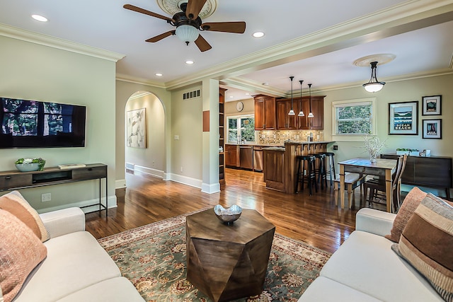 living room with arched walkways, crown molding, dark wood-style flooring, a ceiling fan, and baseboards
