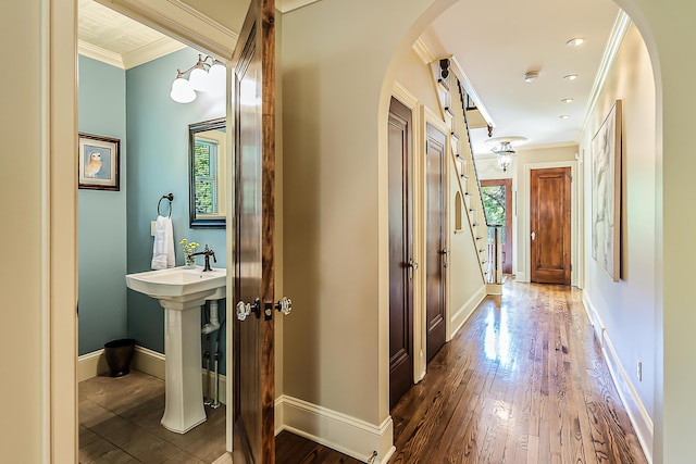 corridor featuring ornamental molding, arched walkways, wood finished floors, and baseboards