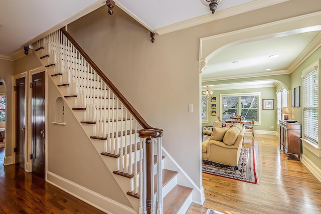 stairway featuring arched walkways, plenty of natural light, wood finished floors, a chandelier, and ornamental molding