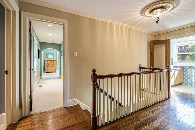 hallway with an upstairs landing, wood-type flooring, arched walkways, baseboards, and ornamental molding