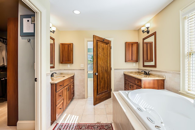 full bath with tile walls, healthy amount of natural light, tile patterned floors, two vanities, and a wainscoted wall
