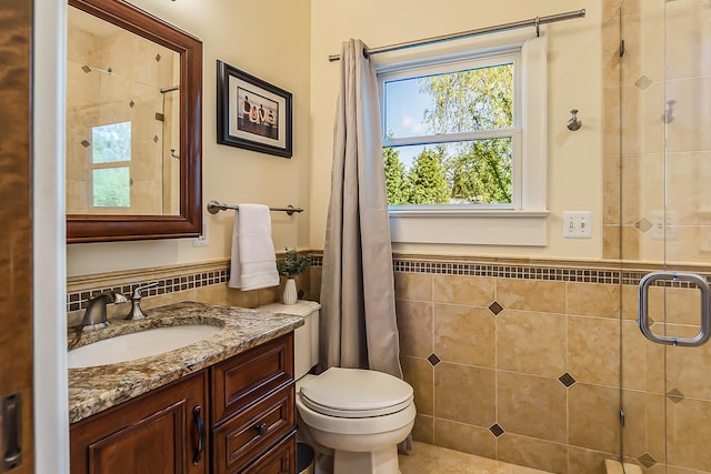 bathroom featuring tile walls, a wainscoted wall, a stall shower, vanity, and toilet