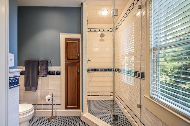 full bath featuring a shower stall, toilet, tile patterned flooring, tile walls, and wainscoting