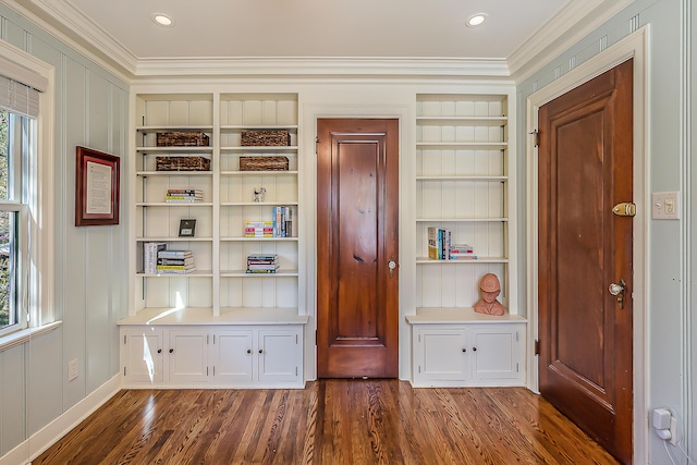 interior space with ornamental molding, built in shelves, wood finished floors, and baseboards