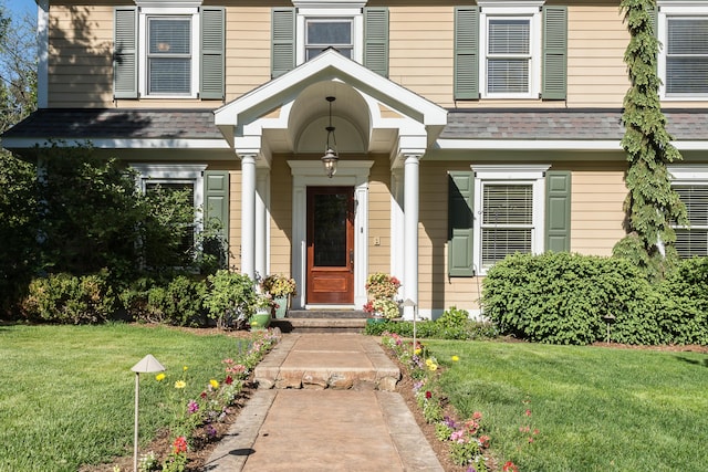 entrance to property with a lawn and a shingled roof