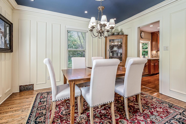 dining room with ornamental molding, wood finished floors, healthy amount of natural light, a chandelier, and a decorative wall