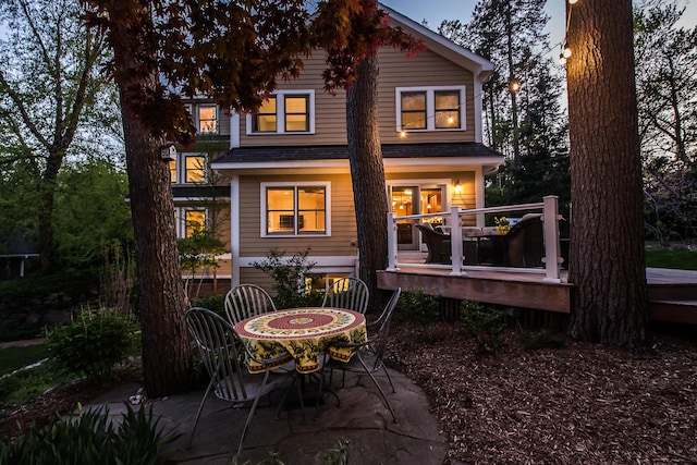 back of property with a deck, roof with shingles, and a patio