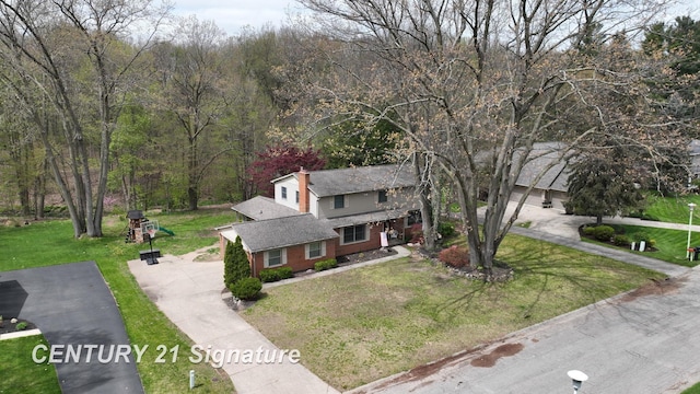 traditional home featuring a front yard, driveway, brick siding, and a forest view