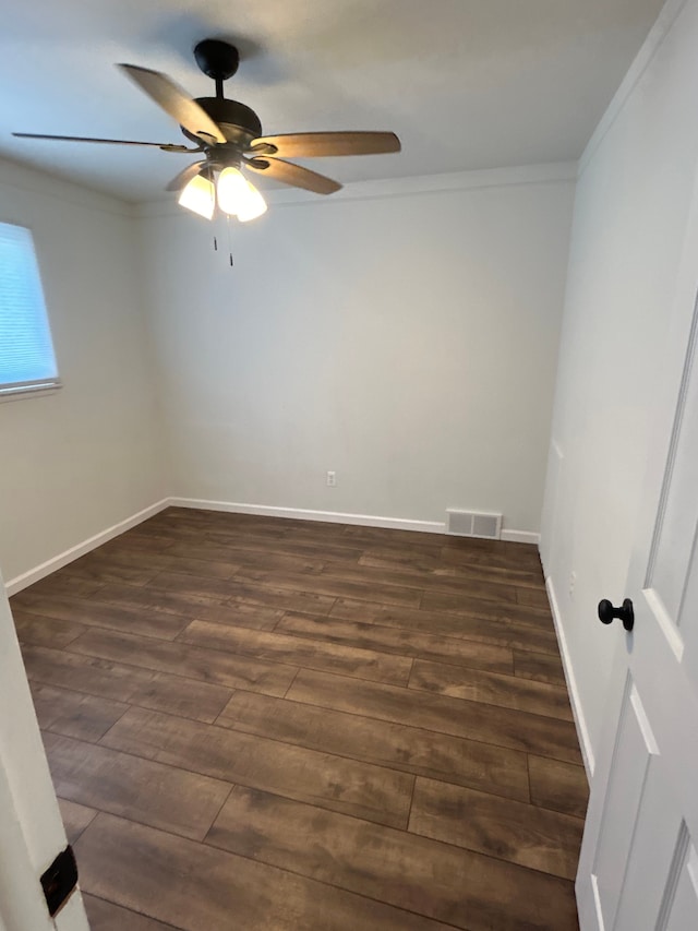 empty room featuring a ceiling fan, crown molding, dark wood finished floors, and baseboards