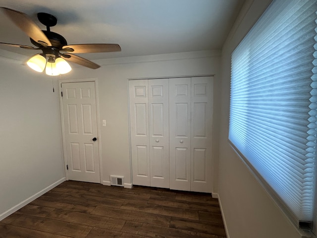 unfurnished bedroom featuring dark wood-style flooring, baseboards, a closet, and a ceiling fan
