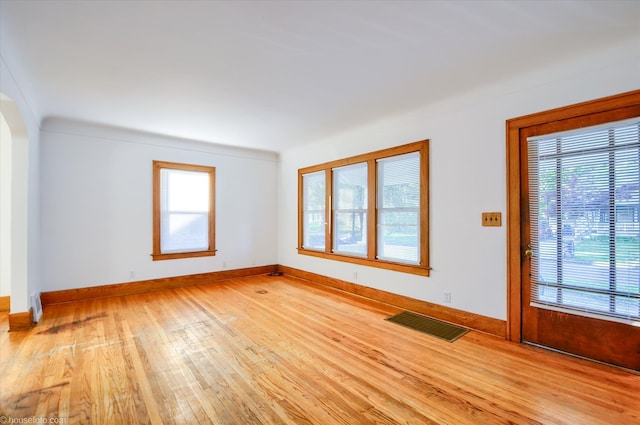 empty room with light wood finished floors, baseboards, and arched walkways