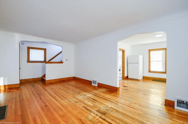 unfurnished living room featuring arched walkways, light wood-type flooring, and baseboards