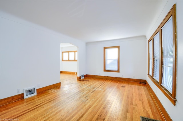 spare room with arched walkways, light wood-type flooring, and baseboards