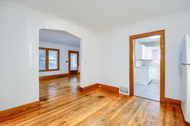 unfurnished room with arched walkways, light wood-type flooring, and baseboards