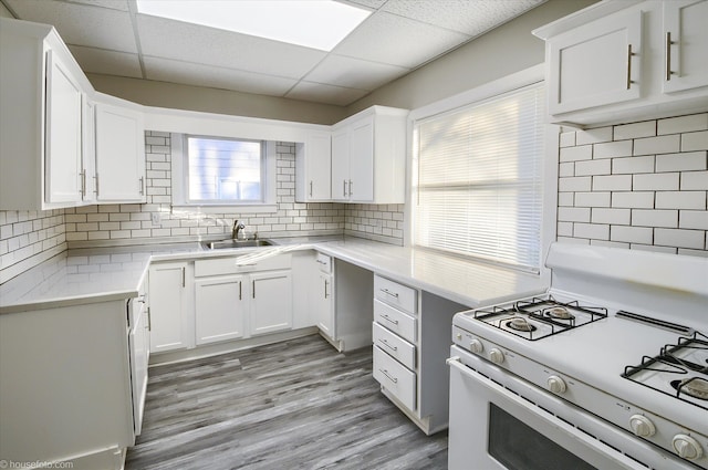 kitchen with white range with gas stovetop, a sink, white cabinetry, backsplash, and light countertops