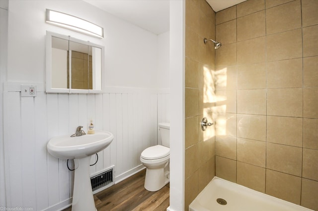 full bathroom featuring wood finished floors, toilet, a stall shower, a wainscoted wall, and a sink