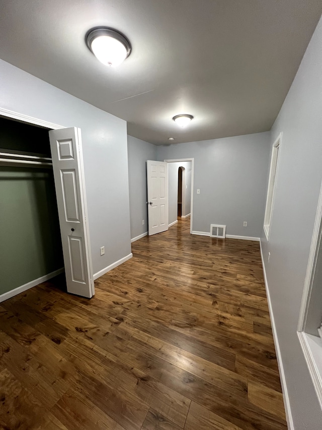 unfurnished bedroom with dark wood finished floors, baseboards, and a closet
