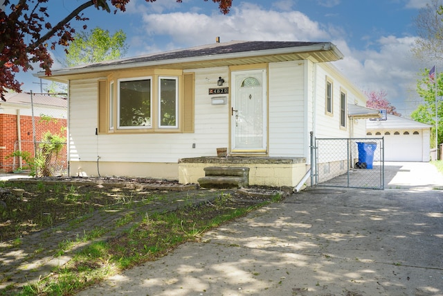 bungalow-style house with concrete driveway, fence, a gate, a garage, and an outdoor structure