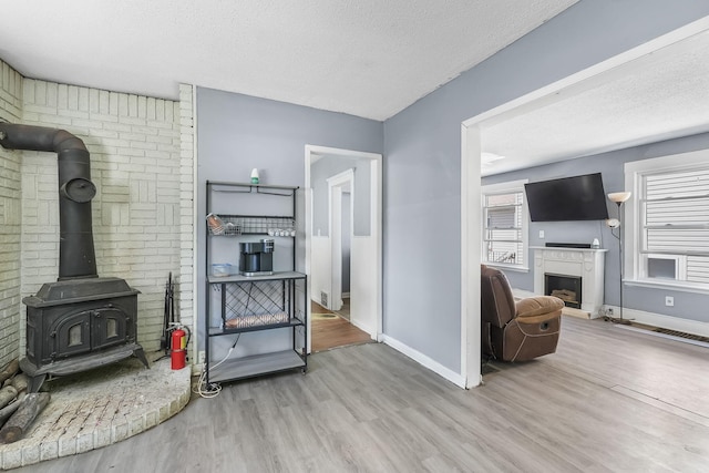 living area featuring baseboards, wood finished floors, a textured ceiling, a wood stove, and a fireplace