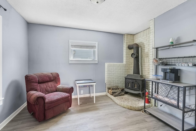 living area with wood finished floors, a wood stove, a textured ceiling, and baseboards