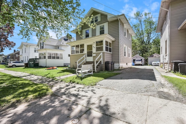 traditional style home with entry steps, asphalt driveway, an outdoor structure, a front yard, and a detached garage