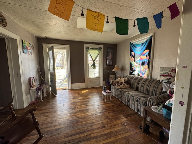 living area with a drop ceiling, hardwood / wood-style flooring, and baseboards