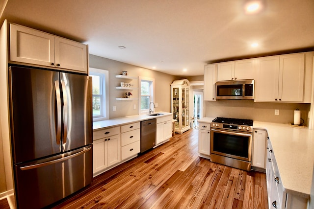 kitchen with appliances with stainless steel finishes, open shelves, light countertops, recessed lighting, and wood finished floors