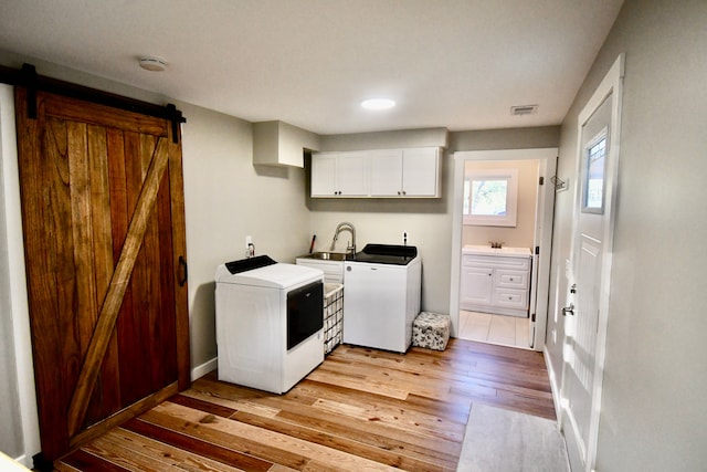 laundry room featuring washer and clothes dryer, a barn door, light wood-style flooring, cabinet space, and baseboards