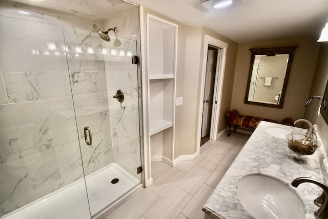 bathroom featuring a marble finish shower, baseboards, and double vanity