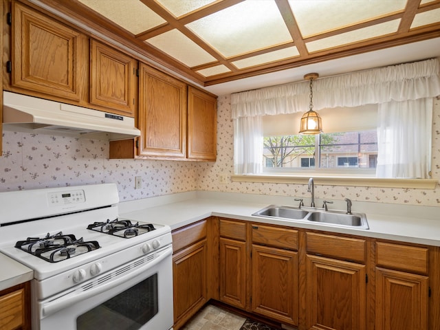 kitchen with white gas range, under cabinet range hood, a sink, brown cabinetry, and light countertops