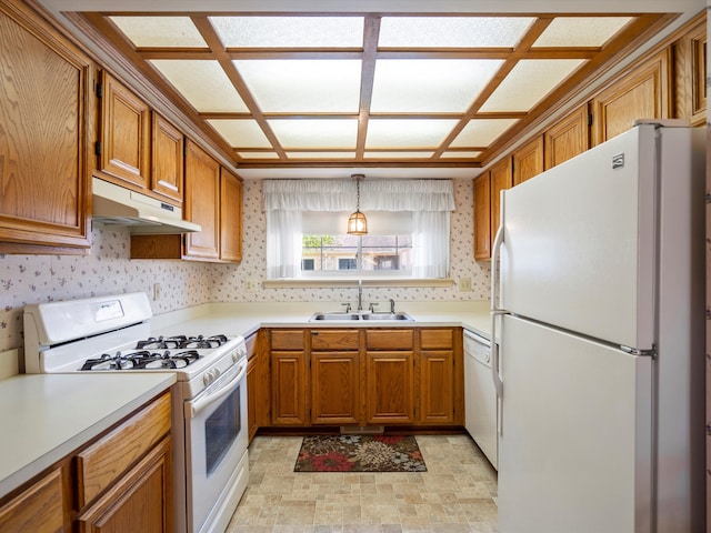kitchen with white appliances, under cabinet range hood, a sink, brown cabinets, and wallpapered walls