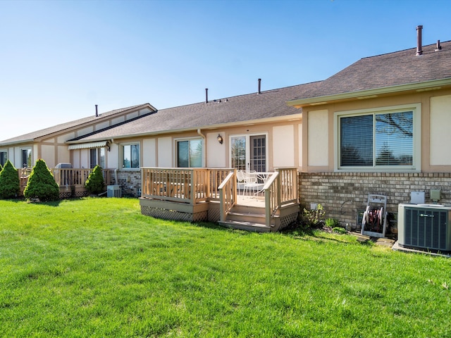 rear view of property with central AC unit, stucco siding, a deck, a lawn, and brick siding