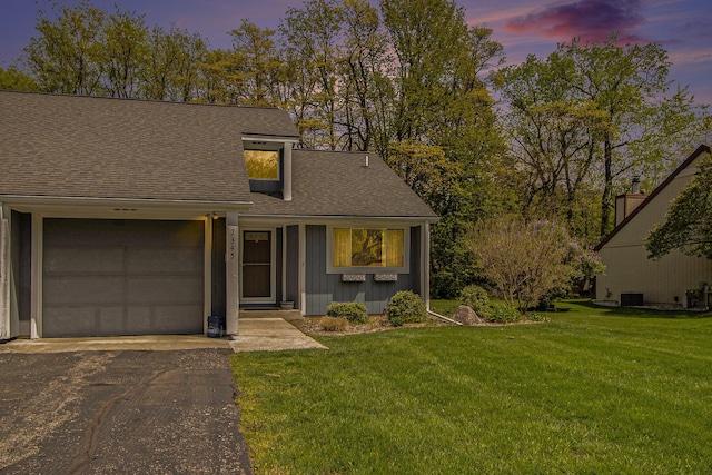 mid-century modern home with roof with shingles, a garage, asphalt driveway, and a yard