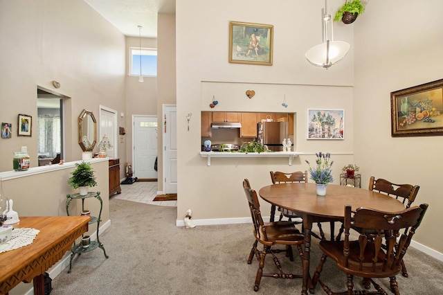 dining room with a towering ceiling, light carpet, and baseboards
