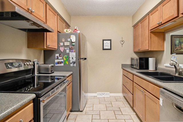 kitchen with appliances with stainless steel finishes, under cabinet range hood, a sink, a textured ceiling, and baseboards