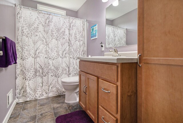 full bath featuring toilet, vanity, stone finish flooring, baseboards, and curtained shower