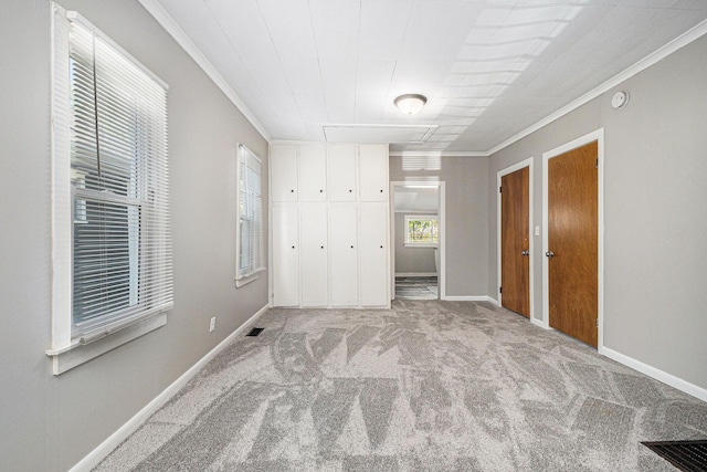 unfurnished bedroom featuring crown molding, carpet, attic access, baseboards, and a closet
