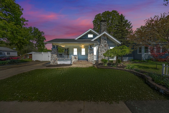 view of front of property with stone siding, covered porch, a chimney, and concrete driveway