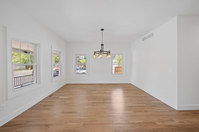 unfurnished dining area with a chandelier, light wood-style floors, and baseboards