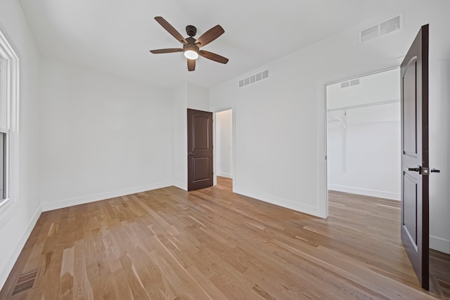 unfurnished bedroom featuring light wood-style floors, baseboards, ceiling fan, and a walk in closet